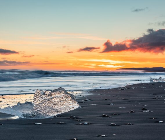 Ice pieces on a black beach shining during sunset.