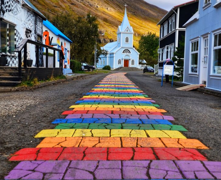 Rainbow street going to a beautiful blue church.
