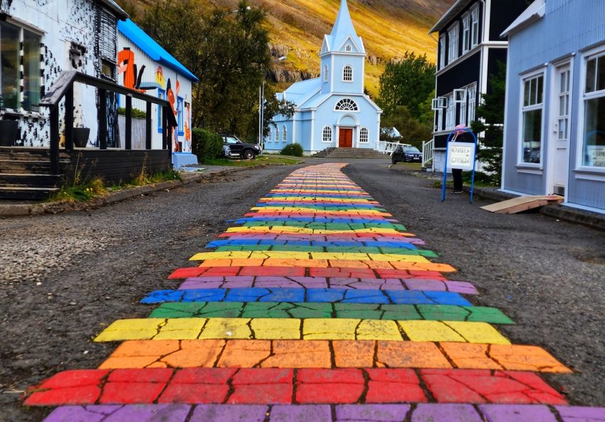 Rainbow street going to a beautiful blue church.